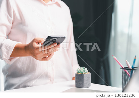 Close-up shot, woman sits at a wooden table using her smartphone, with her finger touching the phone screen as she navigates mobile banking, online shopping, and social media networks. 130123230