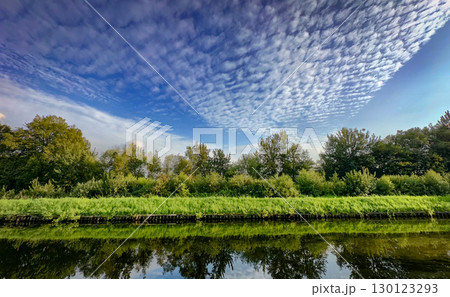 A calm and serene river reflects the landscape under an overcast and cloudy sky 130123293