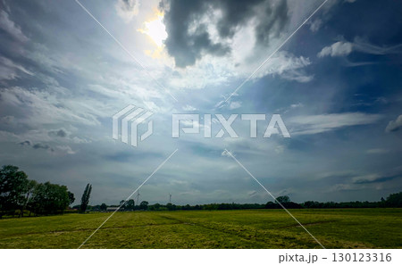 Expansive Landscape Featuring a Dramatic Sky Above Vibrant and Lush Green Fields Expansive Landscape Featuring a Dramatic Sky Above Vibrant and Lush Green Fields 130123316