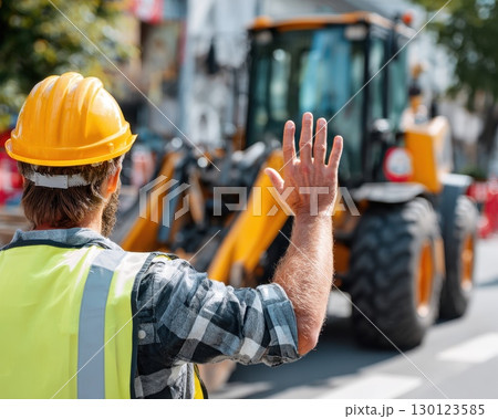 A man in a yellow safety vest is waving to a large construction vehicle 130123585