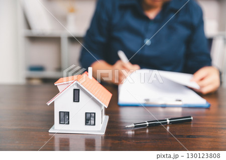 House model placed on table alongside coins, paperwork symbolizes real estate investment, property valuation, representing financial planning, mortgage options, market analysis in property business. 130123808