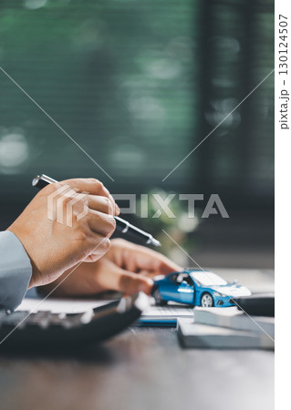 Client is signing the contract and insurance document for the purchase of a vehicle, finalizing finance and loan agreements that mark the approval of a smart investment and successful car deal. 130124507