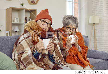 Senior couple sitting wrapped in a blanket trying to warm with a cup of hot tea. 130124657