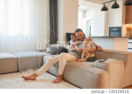 Smiling, positive facial expression. Father with two baby boys is sitting at sofa 130126819