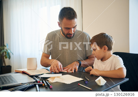 Learning how to craft origami. Father and son are at home by the table Learning how to craft origami. Father and son are at home by the table 130126916