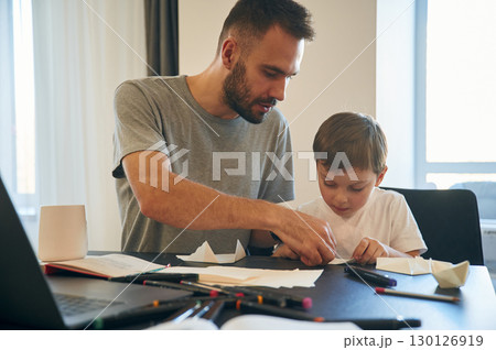 Learning how to craft origami. Father and son are at home by the table 130126919