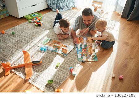 Enjoying board game. Father is playing with two little boys on the floor with toys Enjoying board game. Father is playing with two little boys on the floor with toys 130127105
