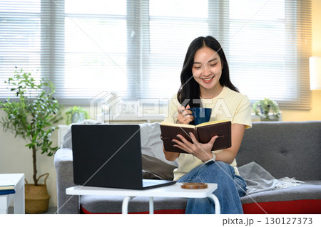 Smiling woman holding notebook and coffee cup while working from home. 130127373
