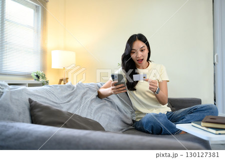 Excited woman holding credit card and smartphone, surprised by online shopping deal 130127381