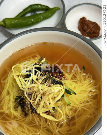 Janchi Guksu, a light and savory Korean noodle dish served in a clear broth, topped with vegetables, egg strips, and seaweed. A simple yet flavorful meal often enjoyed on special occasions. 130127523