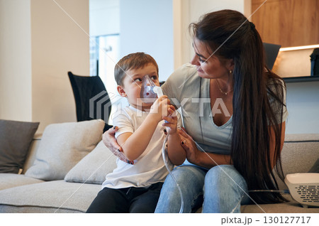 Inhalation for reducing the coughing. Mother with her little son is at home in domestic room 130127717