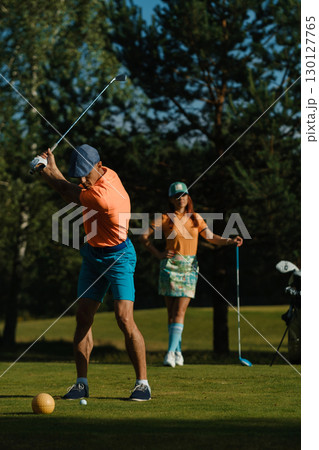 Golfers enjoying a sunny afternoon on a lush course, showcasing swings and style while preparing for a round of golf amidst tall trees Golfers enjoying a sunny afternoon on a lush course, showcasing swings and style while preparing for a round of golf amidst tall trees 130127765