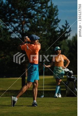 A man hits a ball on a golf course. A couple enjoys a sunny day playing golf on a bright green course 130127768
