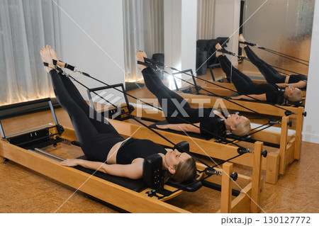 Pilates workout session featuring multiple individuals using reformer machines in a modern studio during afternoon hours 130127772