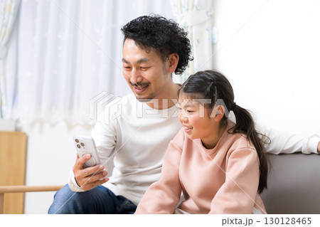 家のソファーで一緒にスマホを見る親子 父親と娘 家のソファーで一緒にスマホを見る親子 父親と娘 130128465