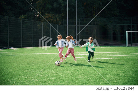Running with ball. Kids are having fun on the green soccer field together 130128844