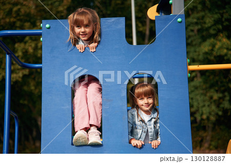 Hiding behind blue construction, smiling. Kids are having fun on the playground Hiding behind blue construction, smiling. Kids are having fun on the playground 130128887