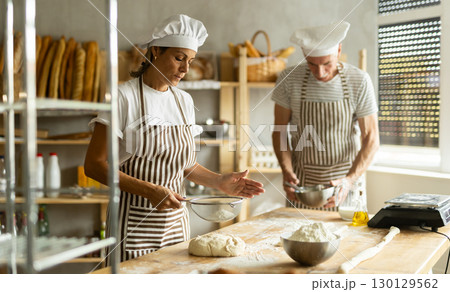Elderly man and woman sift flour and whipping dough 130129562