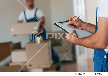 Document in hands. Two moving service employees in a room 130129636