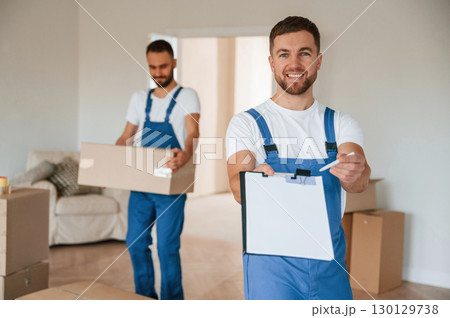 Sign in the documents. Two moving service employees in a room Sign in the documents. Two moving service employees in a room 130129738