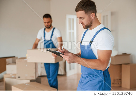 Document in hands. Two moving service employees in a room Document in hands. Two moving service employees in a room 130129740