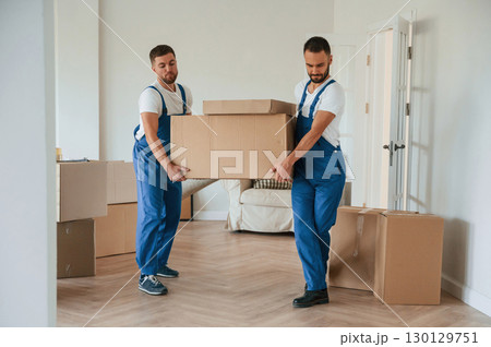 One big heavy box. Two moving service employees in a room One big heavy box. Two moving service employees in a room 130129751