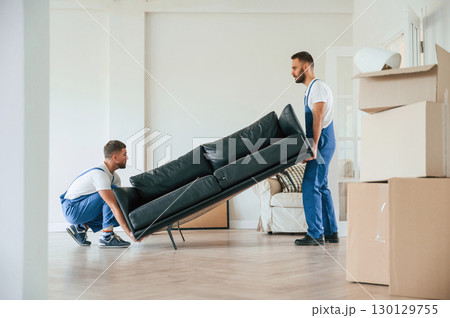 Holding heavy sofa. Two moving service employees in a room Holding heavy sofa. Two moving service employees in a room 130129755