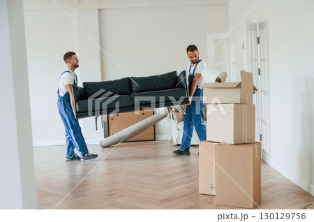 Holding heavy sofa. Two moving service employees in a room Holding heavy sofa. Two moving service employees in a room 130129756