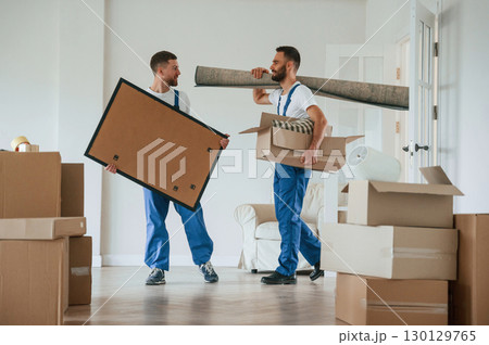 Painting and mat in hands. Two moving service employees in a room 130129765
