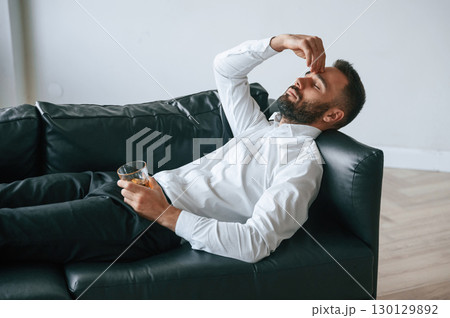 Having headache, lying down on the sofa. Upset young man drinker alcoholic is indoors 130129892