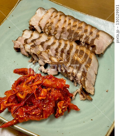 Tender slices of bossam, Korean boiled pork belly, served with fresh lettuce, garlic, and ssamjang. This flavorful and savory dish is perfect for wrapping and sharing in a traditional Korean meal. 130129931