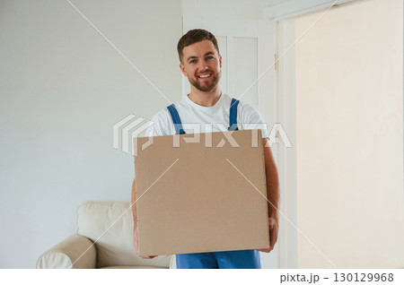 White shirt and blue uniform. With box in hands. Moving service employee in a room 130129968