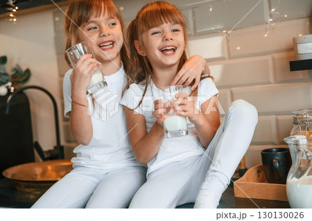 Happy two little girls are drinking milk while sitting on the table on the kitchen 130130026