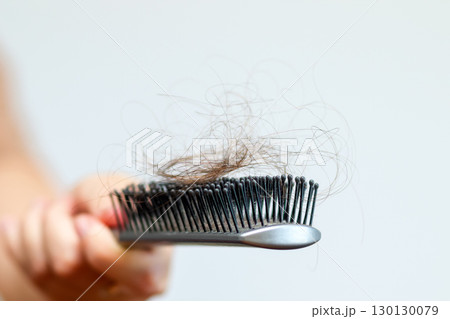 close-up image of a woman's hand holding a comb, with a focus on hair loss and care. hair loss treatment woman comb. female hand holding comb close-up 130130079