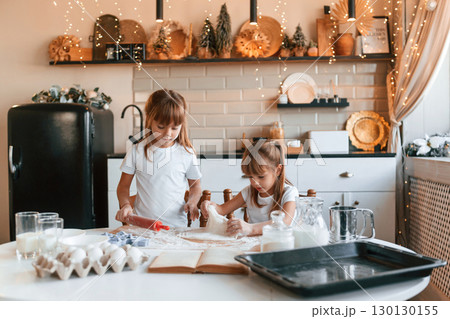 Working with dough. Two little girls are preparing food on the kitchen with garlands 130130155