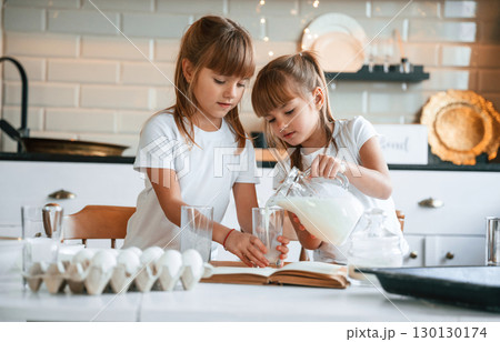 Pouring the milk. Two little girls are preparing food on the kitchen with garlands 130130174