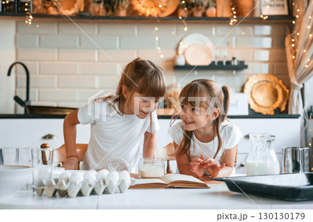 With receipt book. Two little girls are preparing food on the kitchen with garlands 130130179
