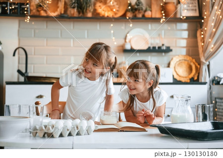 With receipt book. Two little girls are preparing food on the kitchen with garlands With receipt book. Two little girls are preparing food on the kitchen with garlands 130130180