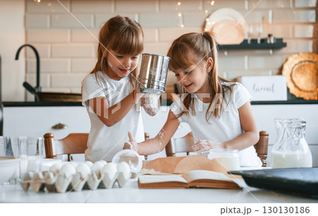Using flour. Two little girls are preparing food on the kitchen with garlands 130130186