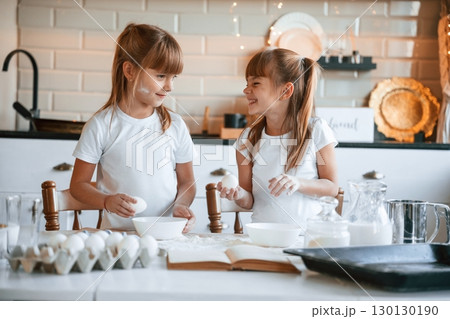 Using flour. Two little girls are preparing food on the kitchen with garlands 130130190
