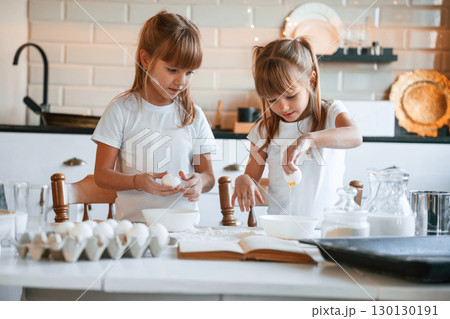 Flour and eggs on the table. Two little girls are preparing food on the kitchen with garlands 130130191