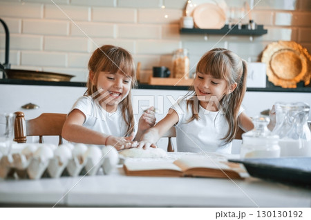 Flour and eggs on the table. Two little girls are preparing food on the kitchen with garlands 130130192