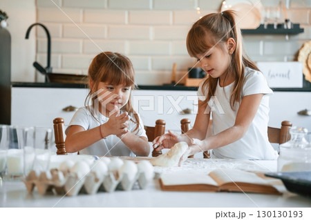 Flour and eggs on the table. Two little girls are preparing food on the kitchen with garlands 130130193