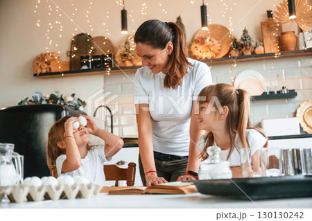 On the kitchen with garlands together. Mother with her little two daughters is preparing food 130130242