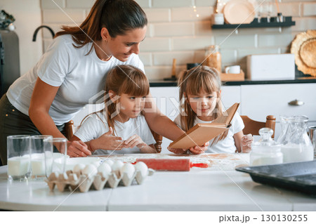 Natural ingredients. Mother with her little two daughters is preparing food on the kitchen with garlands together Natural ingredients. Mother with her little two daughters is preparing food on the kitchen with garlands together 130130255
