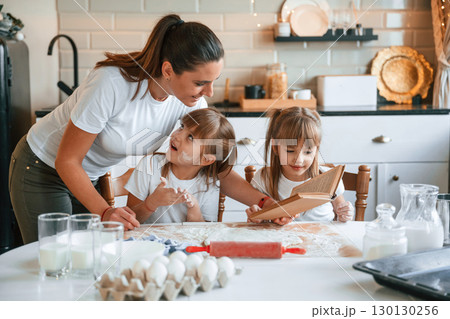Natural ingredients. Mother with her little two daughters is preparing food on the kitchen with garlands together Natural ingredients. Mother with her little two daughters is preparing food on the kitchen with garlands together 130130256