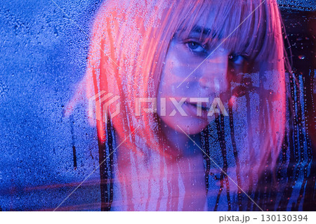 Front view. Stylish woman with white hair is behind wet transparent plastic sheet 130130394