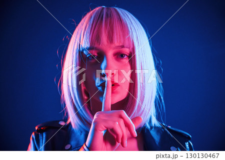 Finger by the lips, silence. Woman with white hair is in studio with neon colors 130130467