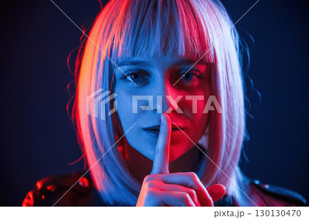 Finger by the lips, silence. Woman with white hair is in studio with neon colors 130130470