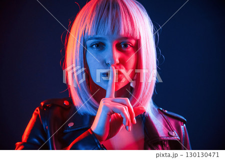 Finger by the lips, silence. Woman with white hair is in studio with neon colors 130130471